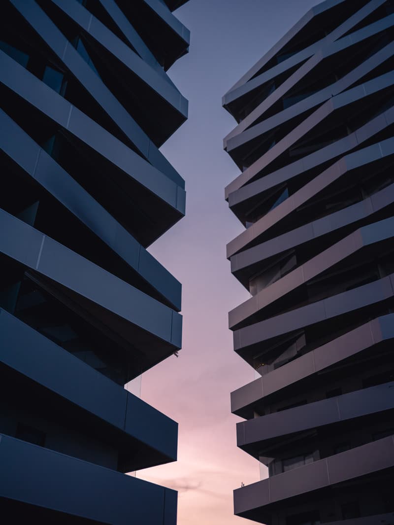 Two dark, angular high-rise buildings framing a narrow strip of sky in soft pink evening light.