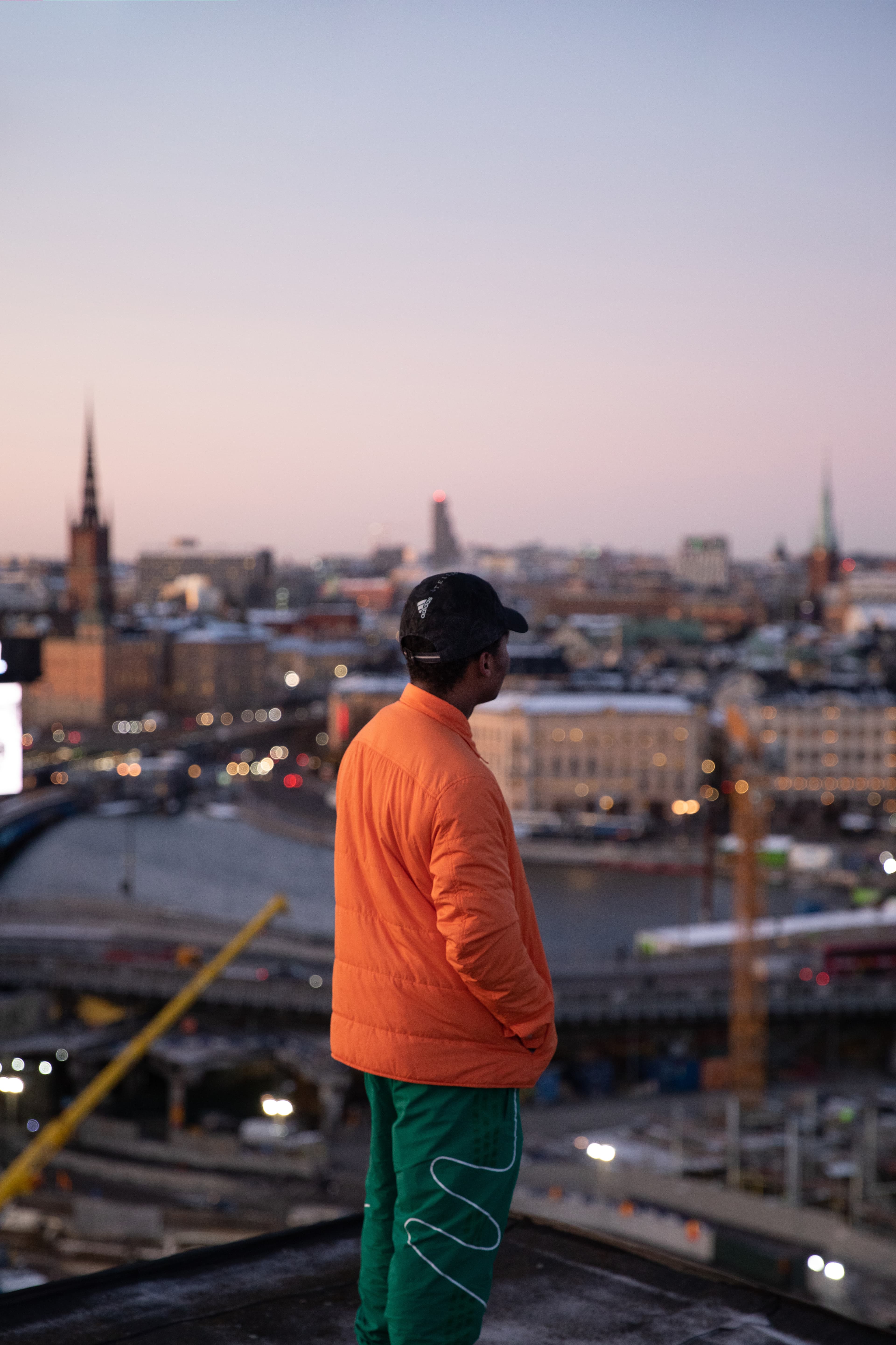 Person in an orange jacket standing on a rooftop, looking out over Stockholm’s skyline in the evening light.