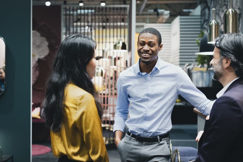 Three people talking and smiling in a modern indoor environment with design furniture and lighting.