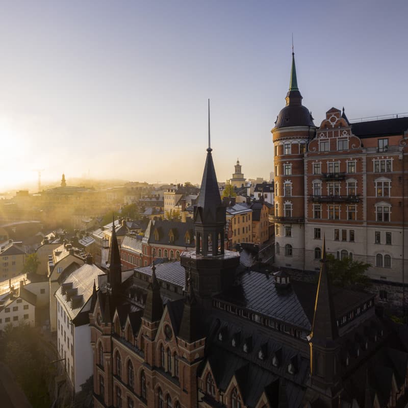 Morning sun over Södermalm rooftops Aerial view of historic buildings and spires in Södermalm, Stockholm, bathed in soft morning light with a hint of mist on the horizon.